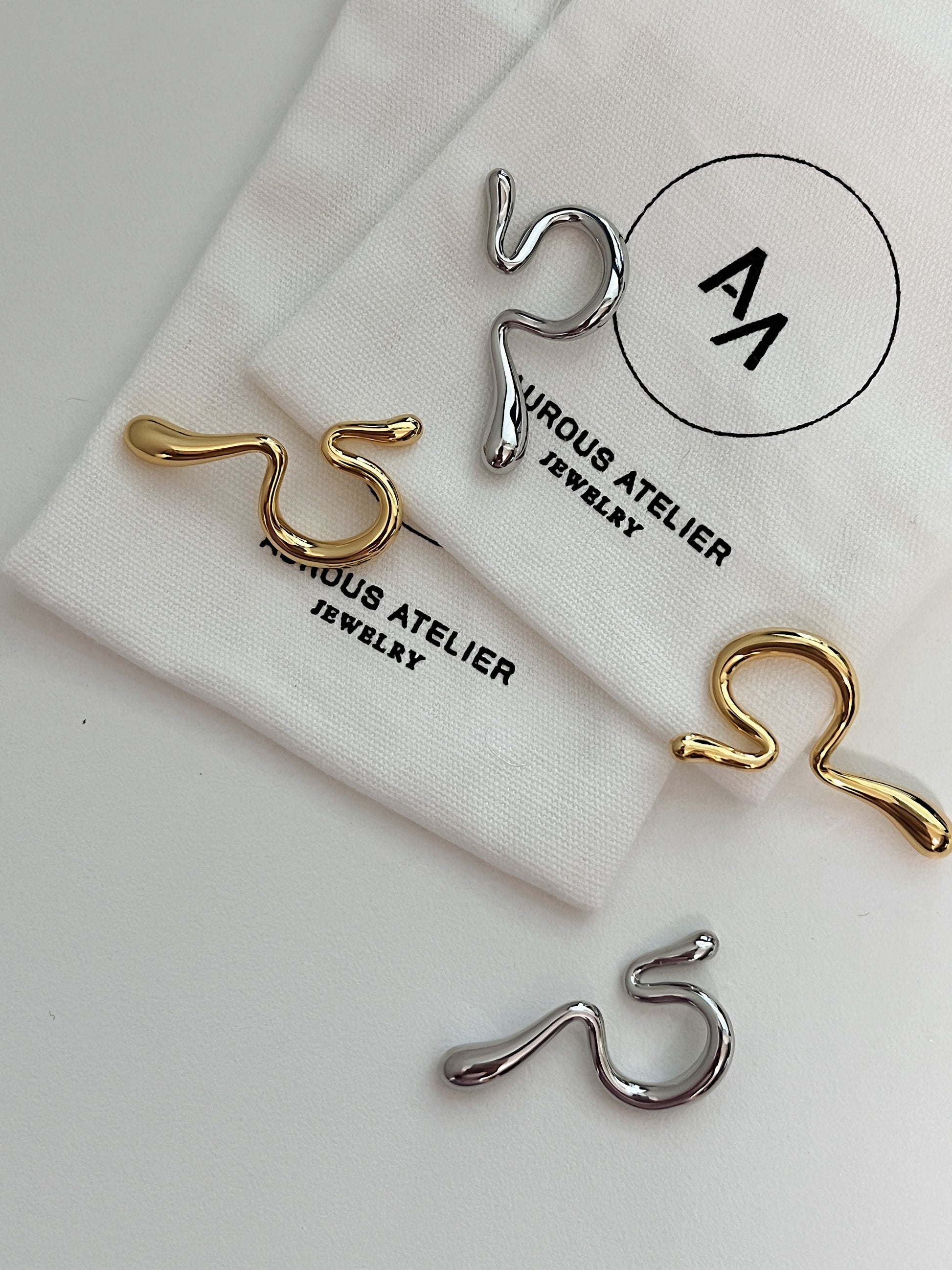 Side-by-side comparison of gold and silver Tia cuffs on a minimalist pedestal.