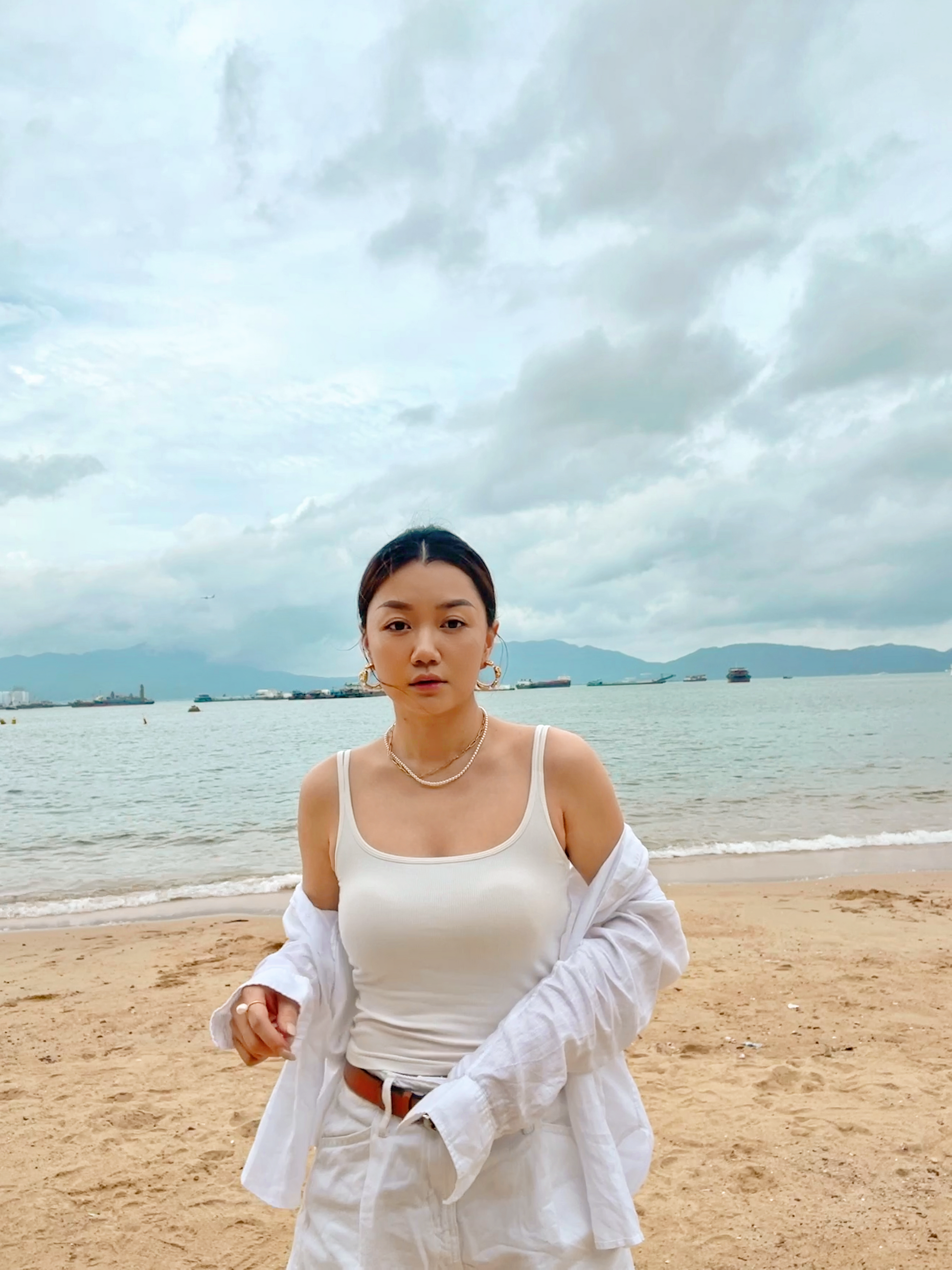 Resort style jewelry lookbook photo of a delicate miniature pearl choker resting on sun warmed skin near crashing waves