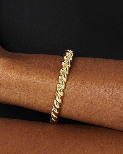 High-contrast studio shot of a model's arm styled with a chunky, twisted croissant gold cuff bracelet emphasizing its reflective, uneven surface.