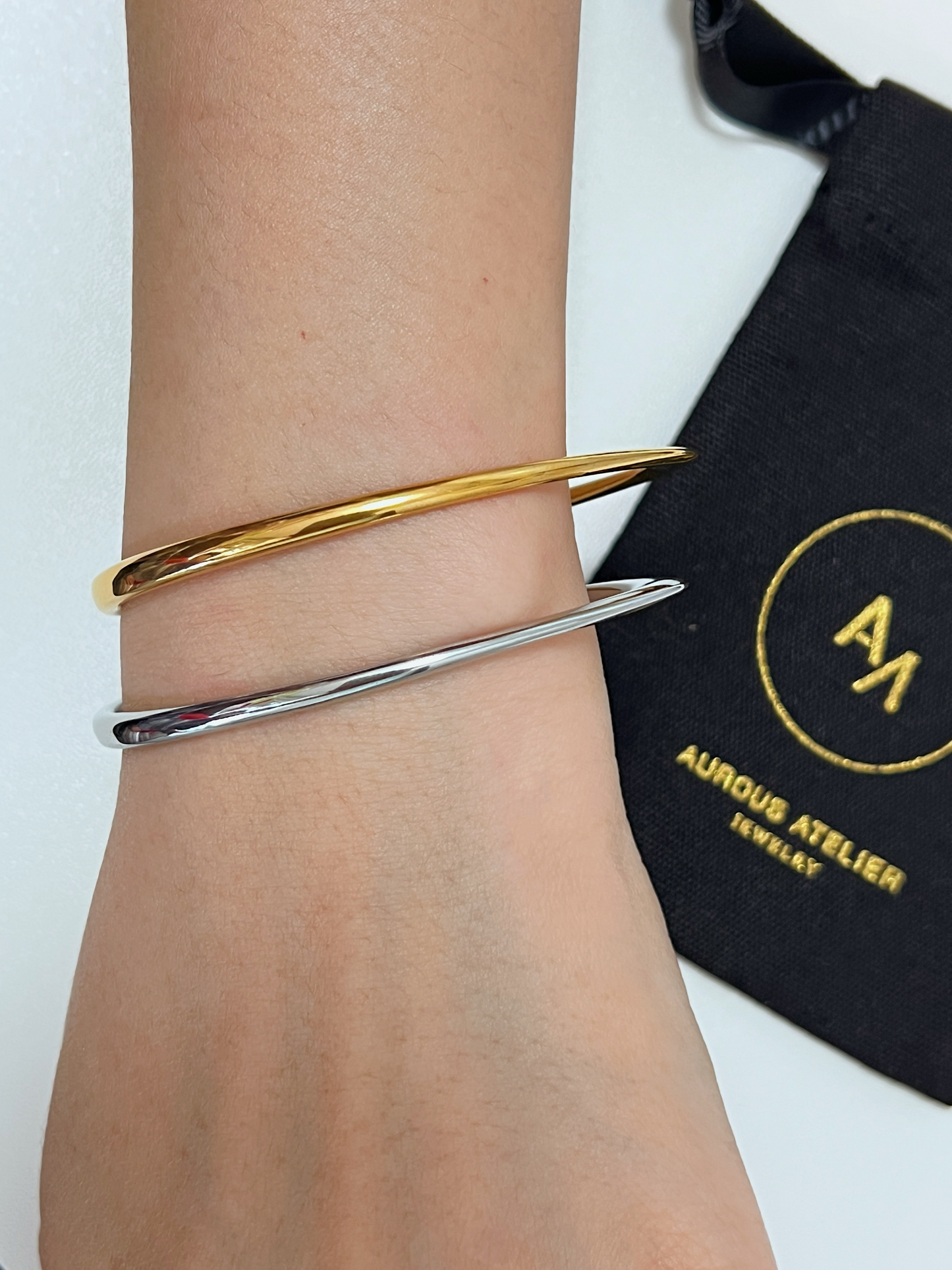 Candid styling shot of a model's arm against a white surface, with the asymmetric gold Iva bangle catching soft lighting.