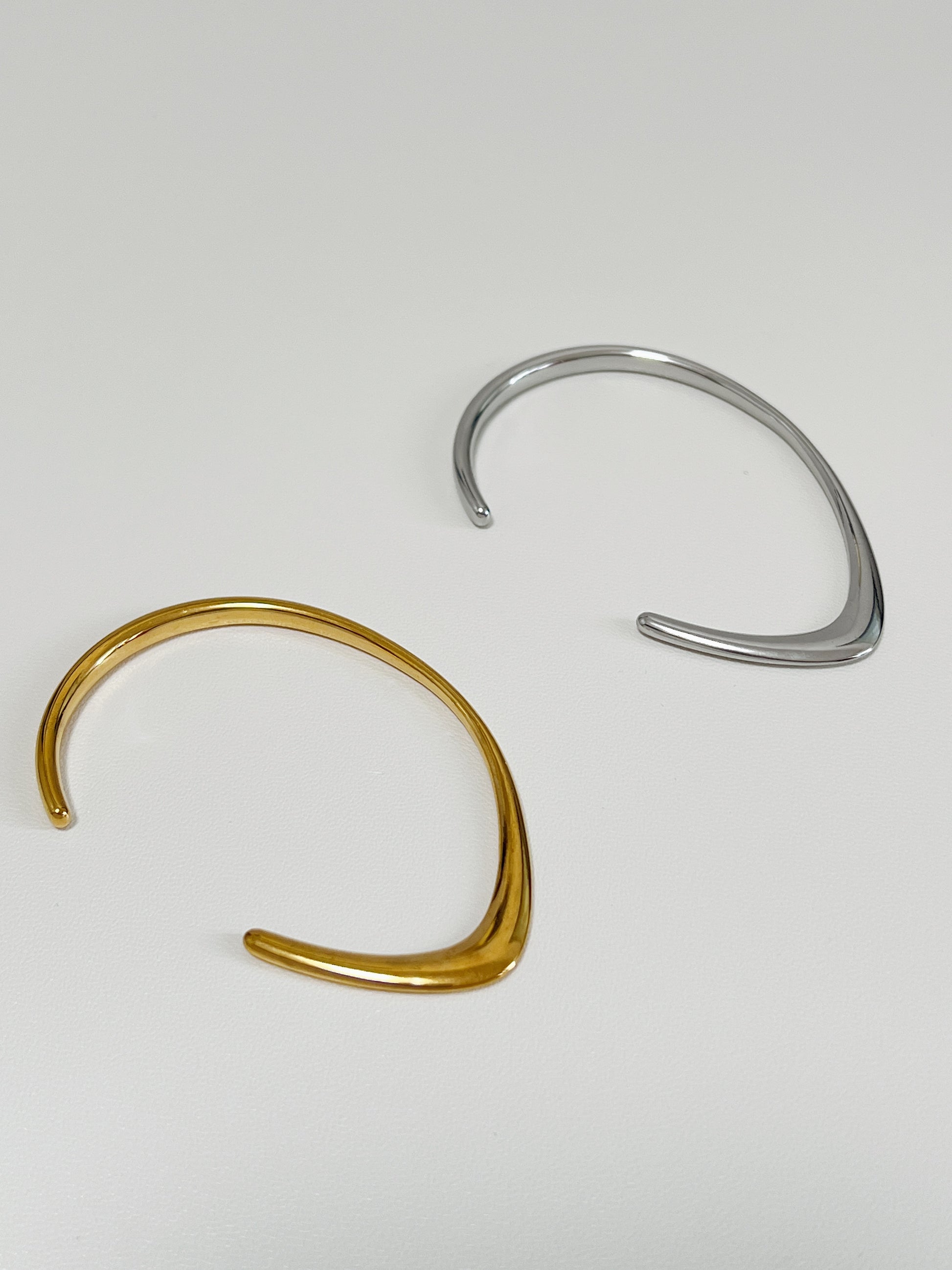 Overhead studio view of the gold and silver Iva undulating metal bangles lying parallel on a clean white surface, showcasing the contrasting ridge and dome profiles of their contours