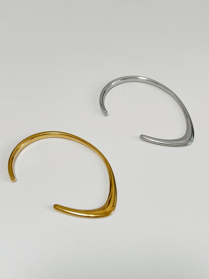 Overhead studio view of the gold and silver Iva undulating metal bangles lying parallel on a clean white surface, showcasing the contrasting ridge and dome profiles of their contours