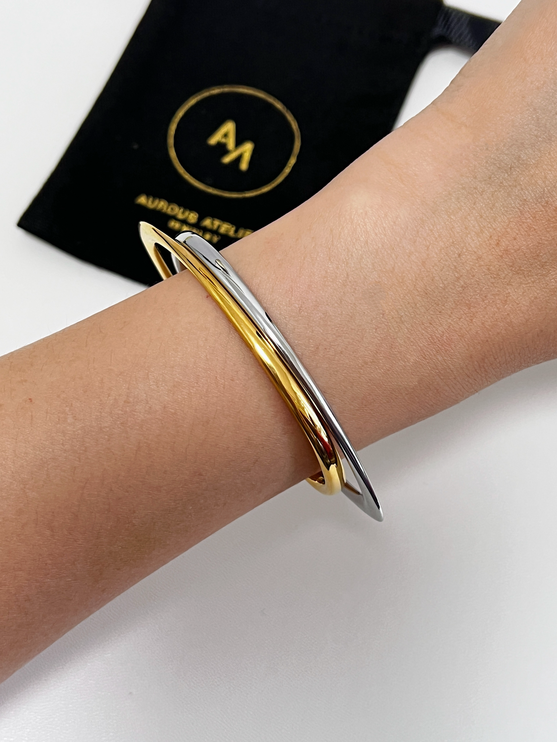 Close-up on-model styling showcasing the gold and silver Iva sculptural irregular bangles layered together on a bare wrist against a clean white background with a black jewelry pouch