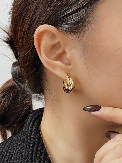 Close-up of model wearing gold Ivette tiered molten clip-on hoop earring with black ribbed knit and dark espresso manicured nails