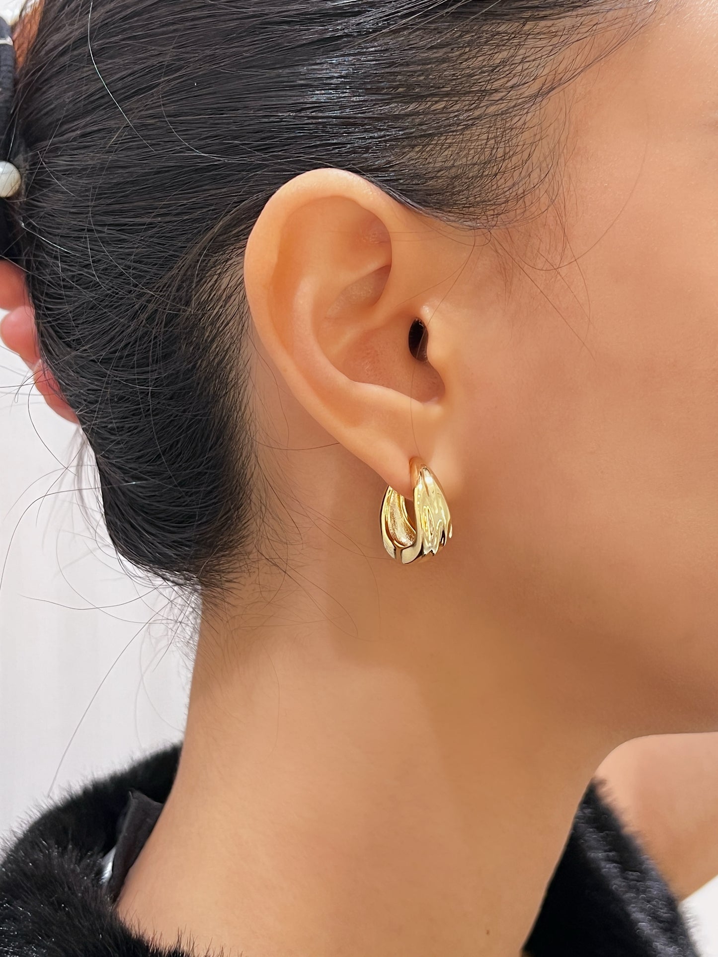 Model wearing 14K gold plated Ivette molten clip-on hoop earring styled with a sleek updo and plush black evening top