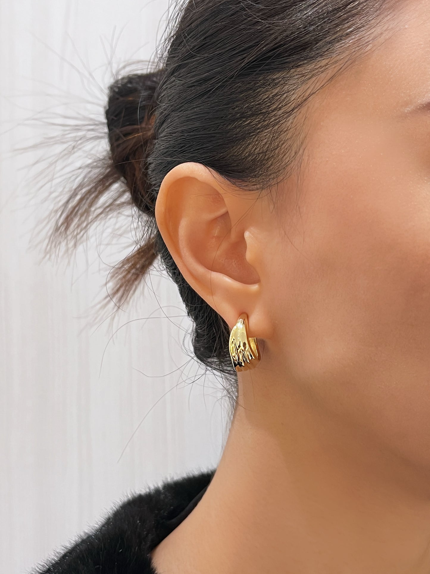 Model wearing Ivette gold clip-on hoops styled with a fur jacket