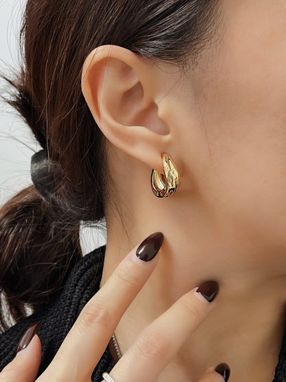 Side profile portrait of model touching neck while wearing gold Ivette molten clip-on hoop earring