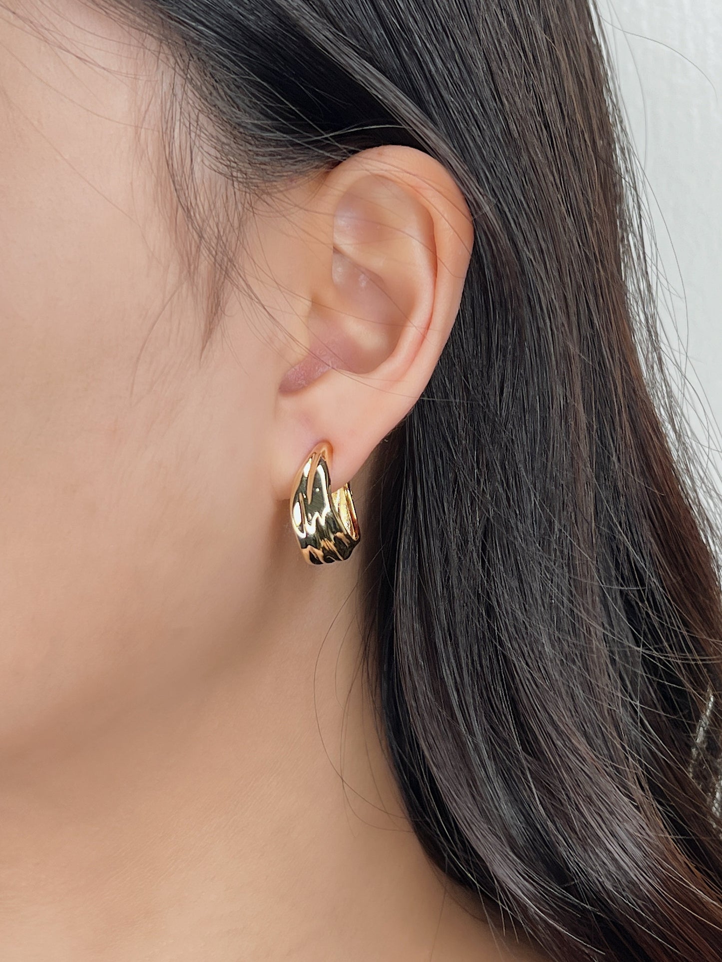 Close-up side profile of model wearing gold Ivette tiered molten clip-on hoop on unpierced earlobe