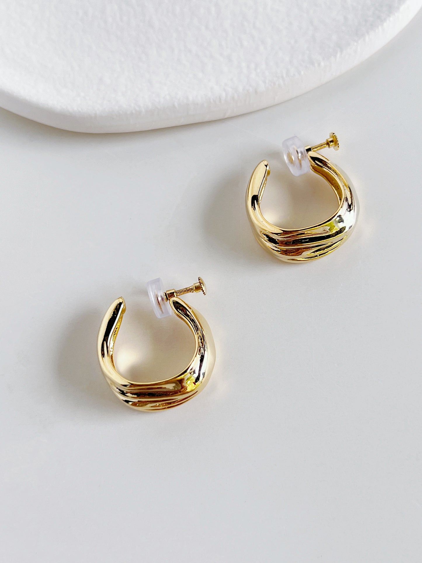 Studio light reflecting off liquid-like molten ridges of gold clip-on hoop earrings