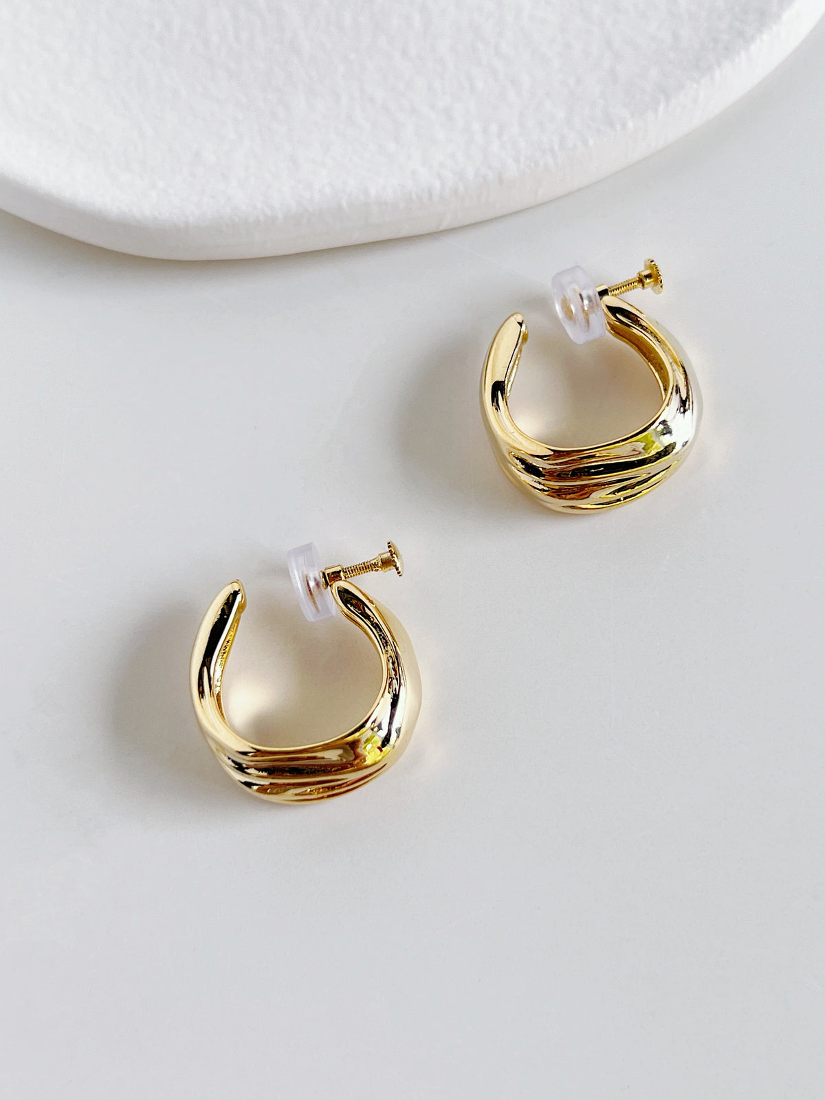 Studio light reflecting off liquid-like molten ridges of gold clip-on hoop earrings