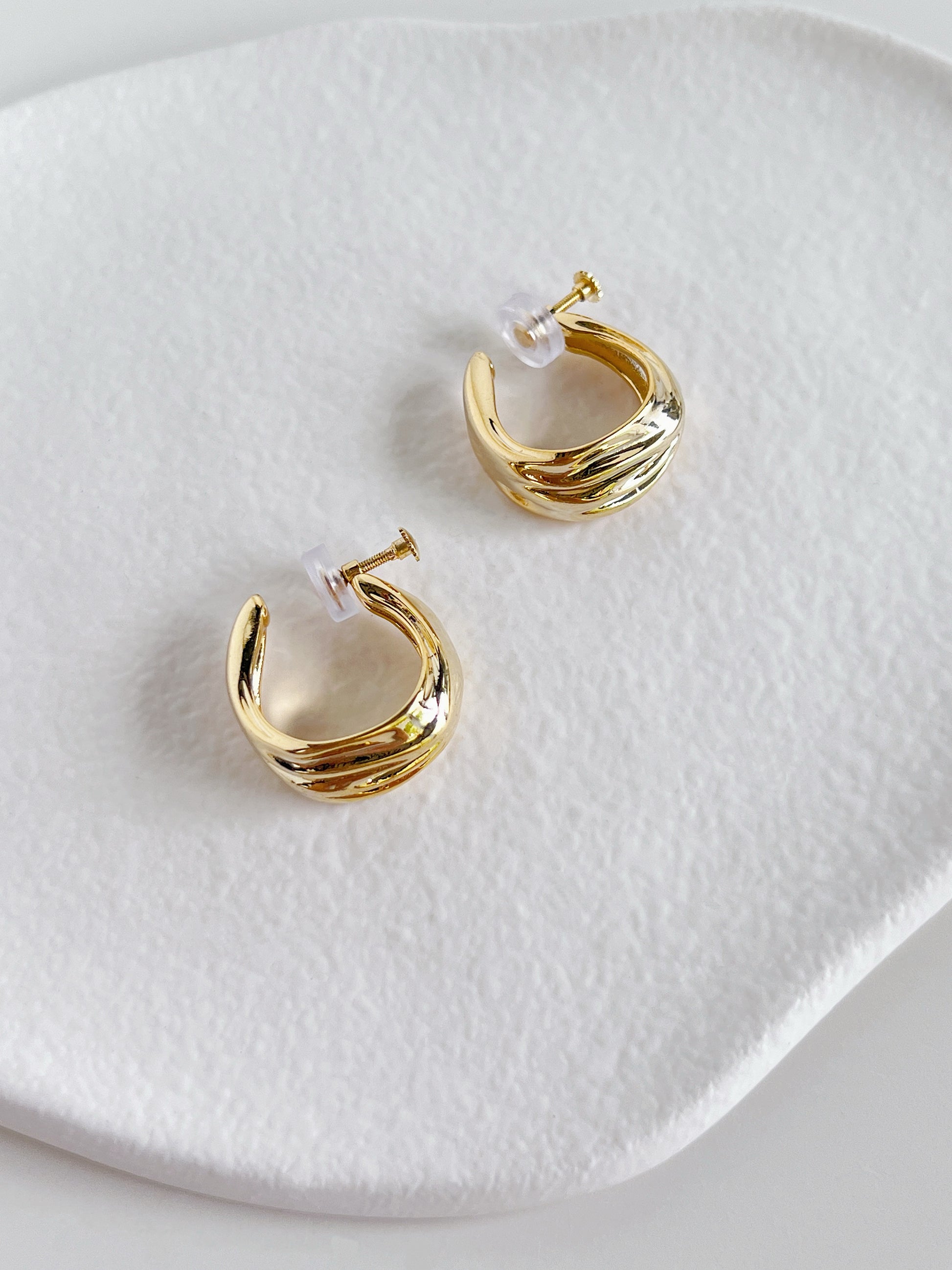 Pair of 14K gold plated Ivette tiered molten clip-on hoop earrings on white background