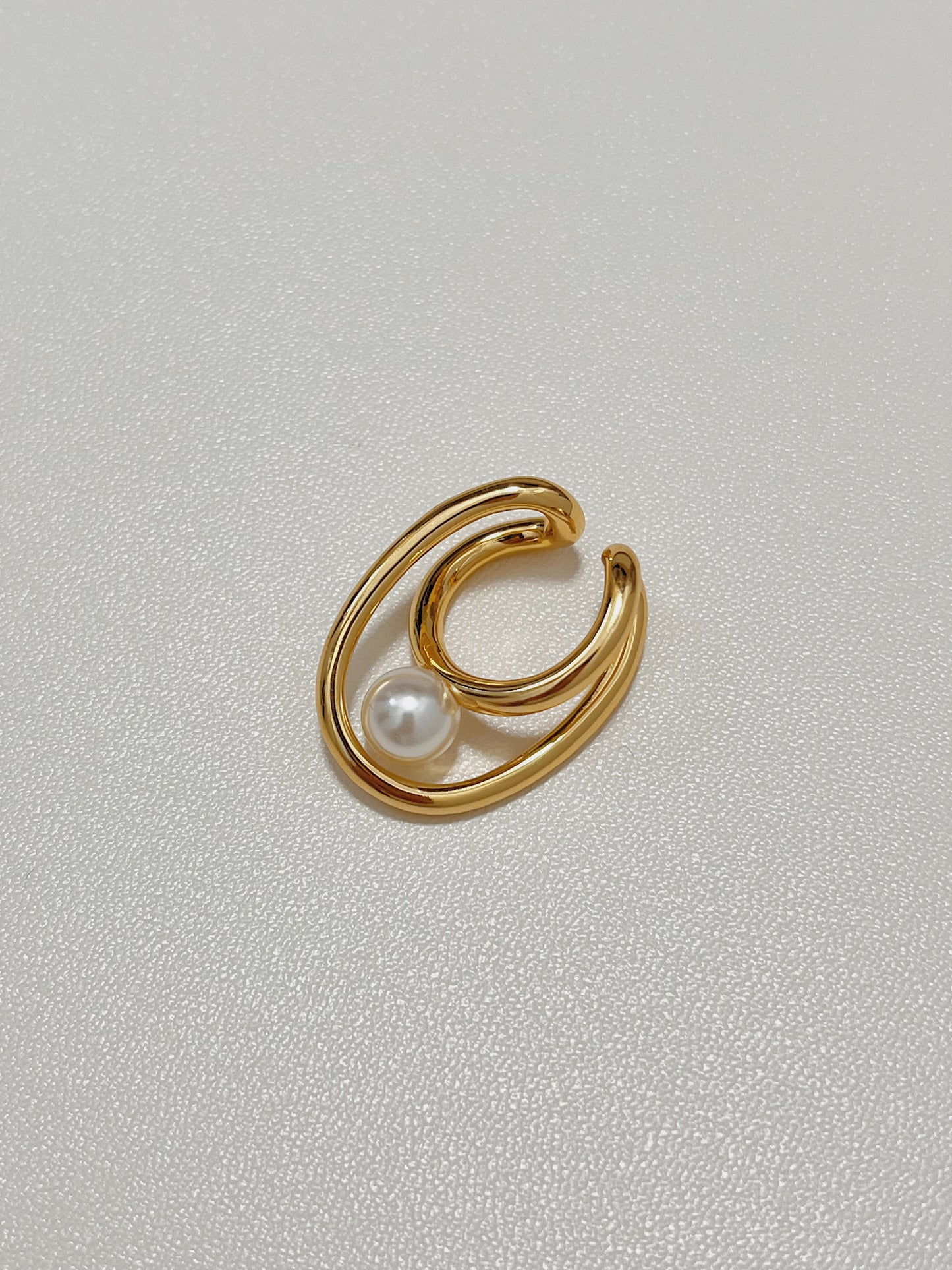 Flat lay close-up of the Karolina Pearl Earlobe Cuff in premium gold plating, highlighting its continuous organic fluid lines and the luminous reflection of its high-luster pearl.