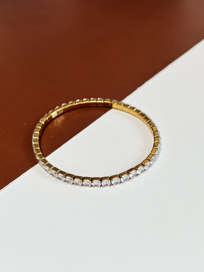 Flat lay view of a gold 4mm elastic tennis bracelet with brilliant cut 5A cubic zirconia stones over a minimalist split-tone background.