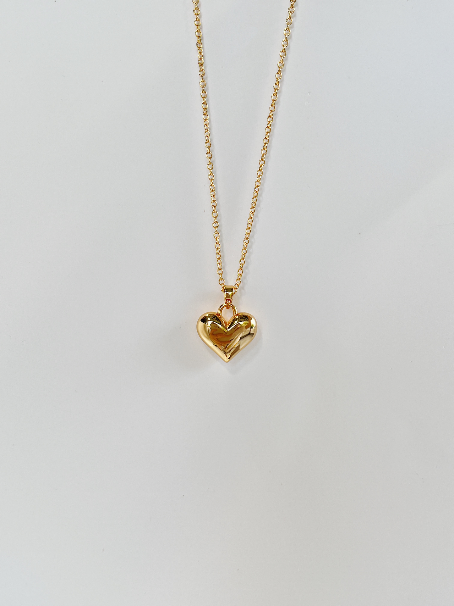 A minimalist jewelry flatlay with the 18k gold PVD Lia heart necklace laid out vertically on white surface