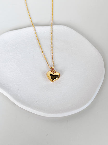 Overhead lifestyle shot of the Lia heart necklace showcasing its solid 3D heart gold pendant resting on a clean white ceramic surface