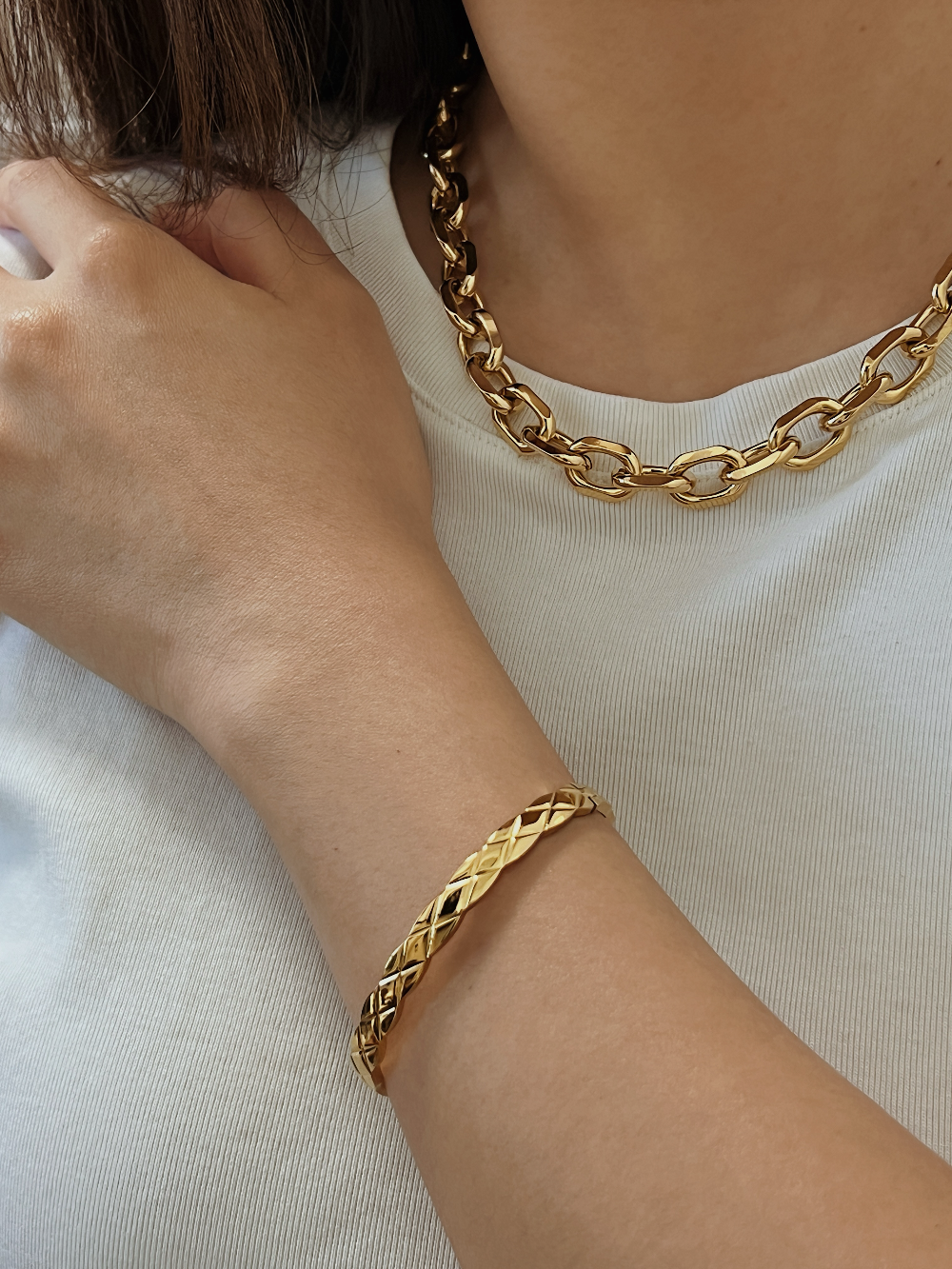 A model styling the textured gold Corin bangle on her wrist, paired harmoniously with a bold, polished gold chain link necklace.
