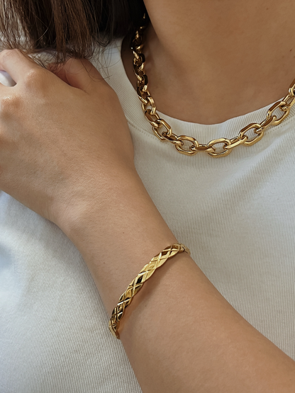 A model styling the textured gold Corin bangle on her wrist, paired harmoniously with a bold, polished gold chain link necklace.