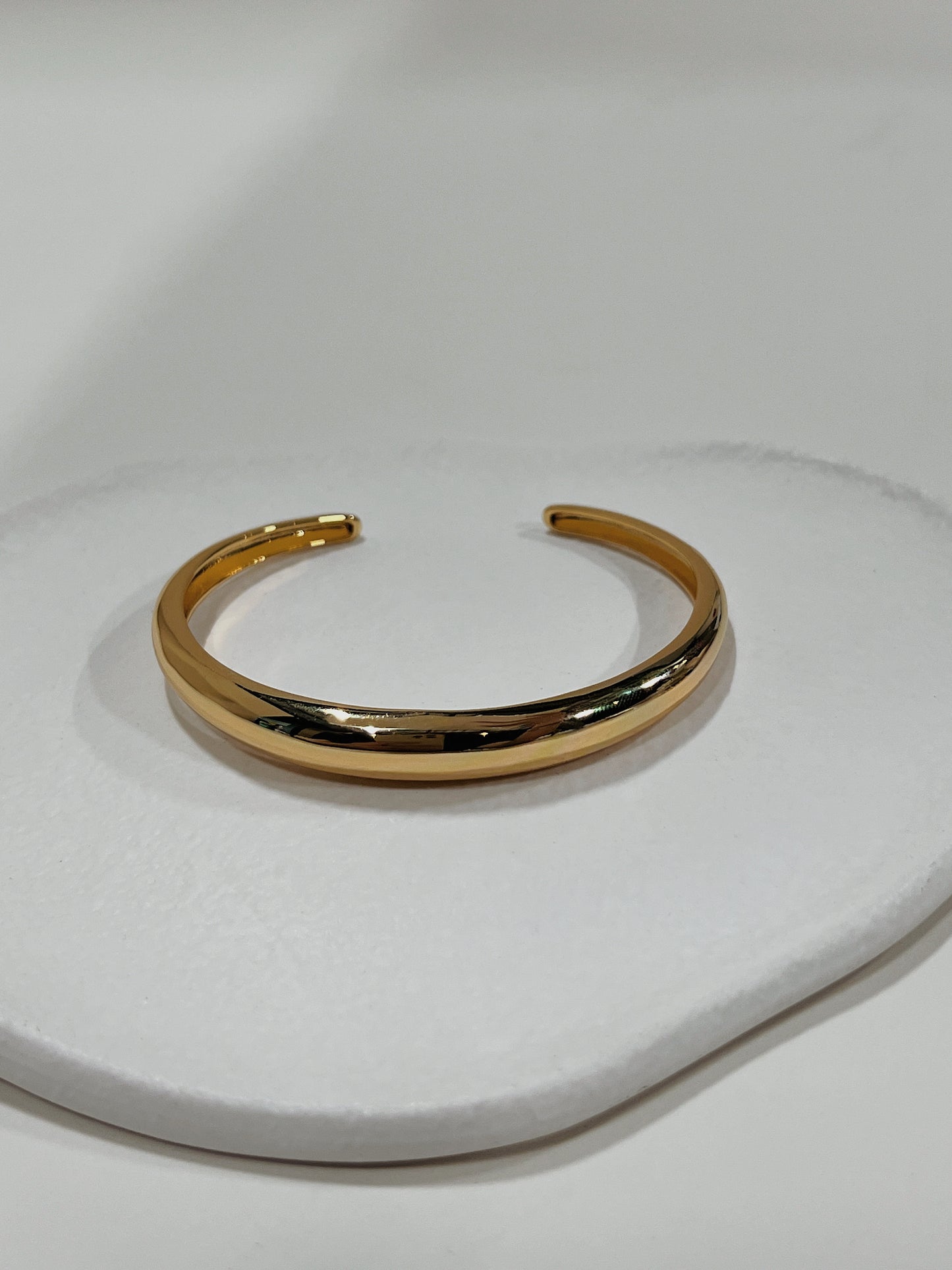 Top-down view of the London Plain minimalist gold open cuff bangle resting on an organic white ceramic plate.