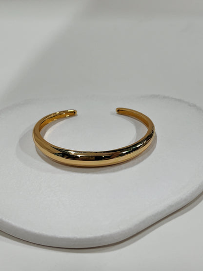 Top-down view of the London Plain minimalist gold open cuff bangle resting on an organic white ceramic plate.