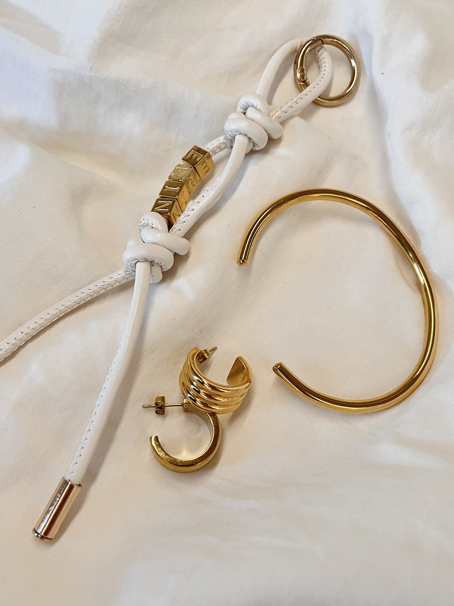 Overhead view of the luxury Lucia Chunky Ribbed Hoop Earrings styled on draped white linen alongside a minimalist gold cuff bracelet.