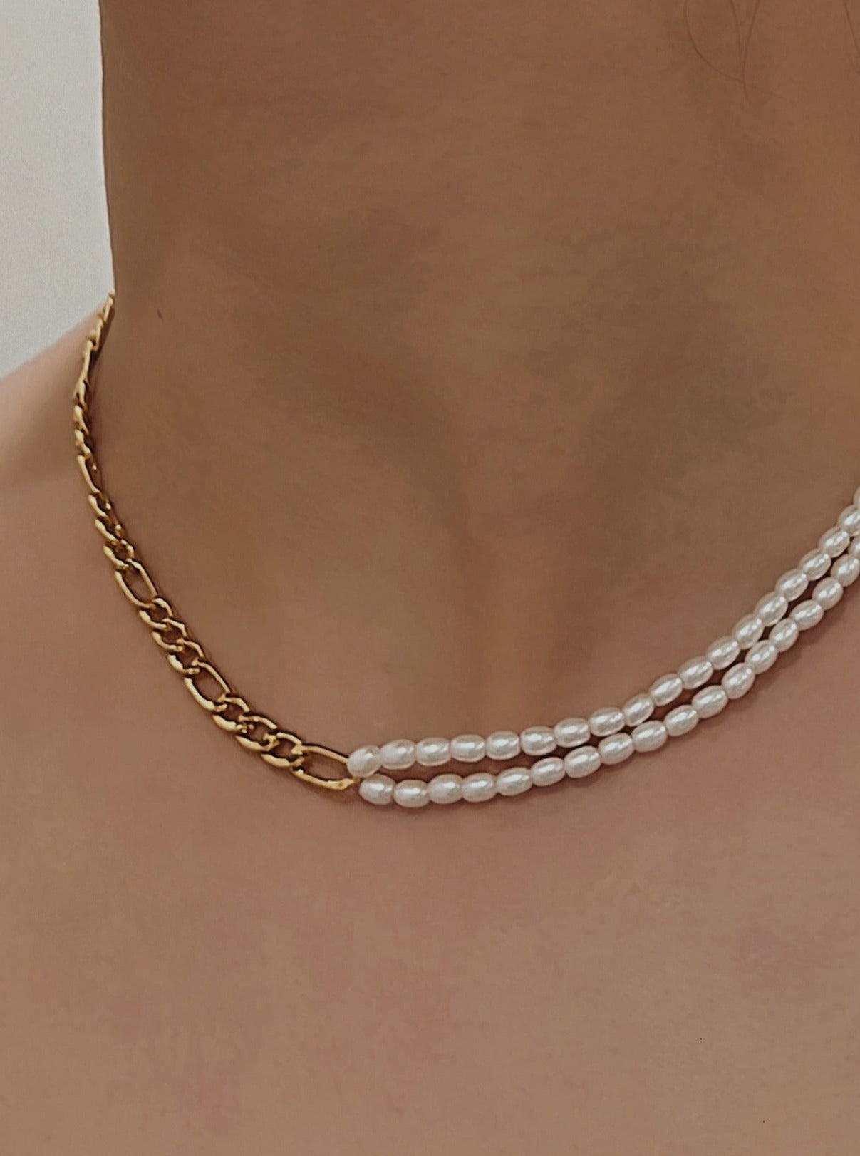 Model view wearing an asymmetrical figaro chain and double row seed pearl necklace