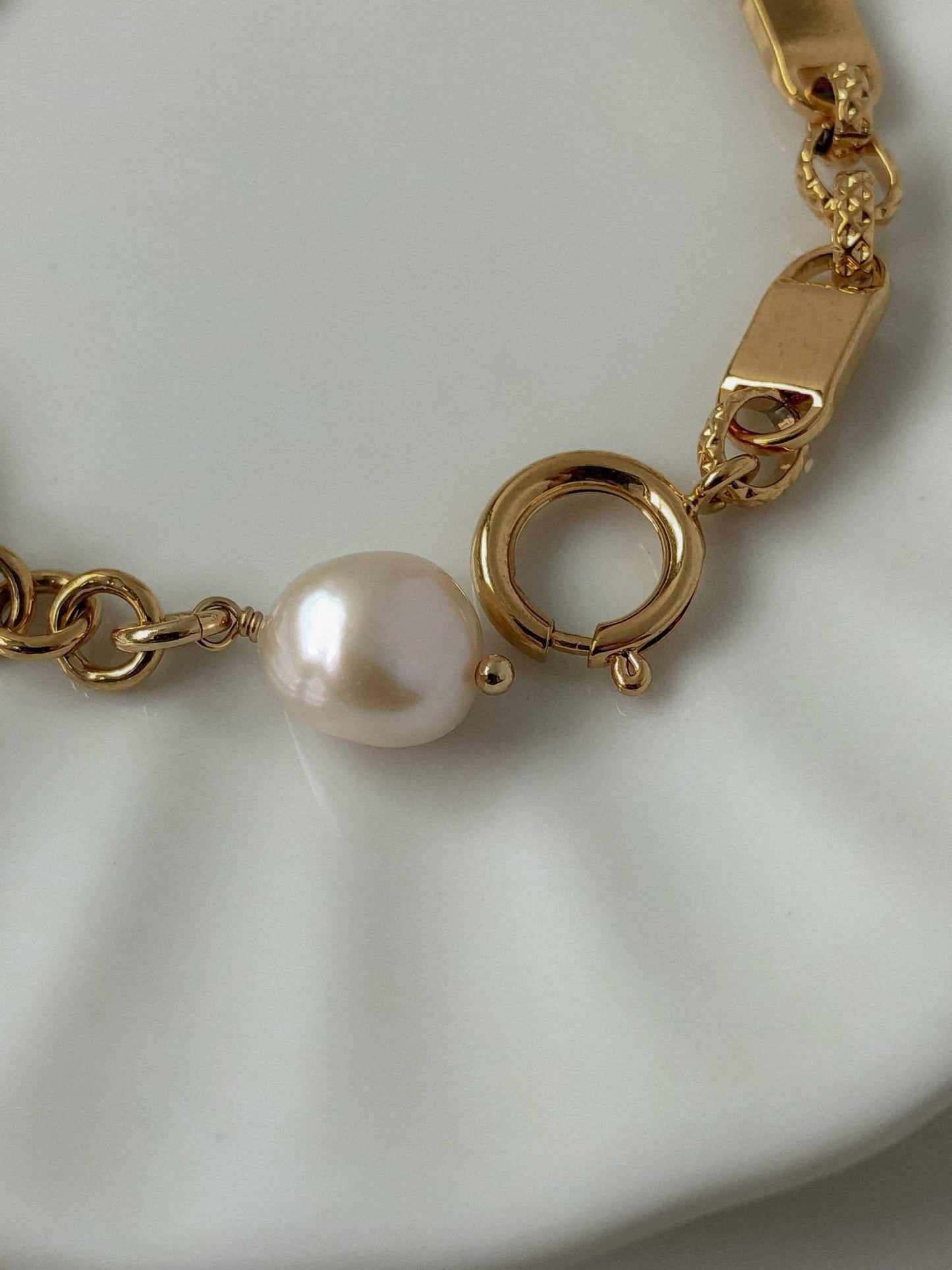 The polished custom spring ring closure and wire-wrapped pearl assembly of the Diana gold link bracelet on a white surface.