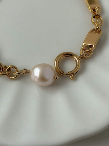 The polished custom spring ring closure and wire-wrapped pearl assembly of the Diana gold link bracelet on a white surface.