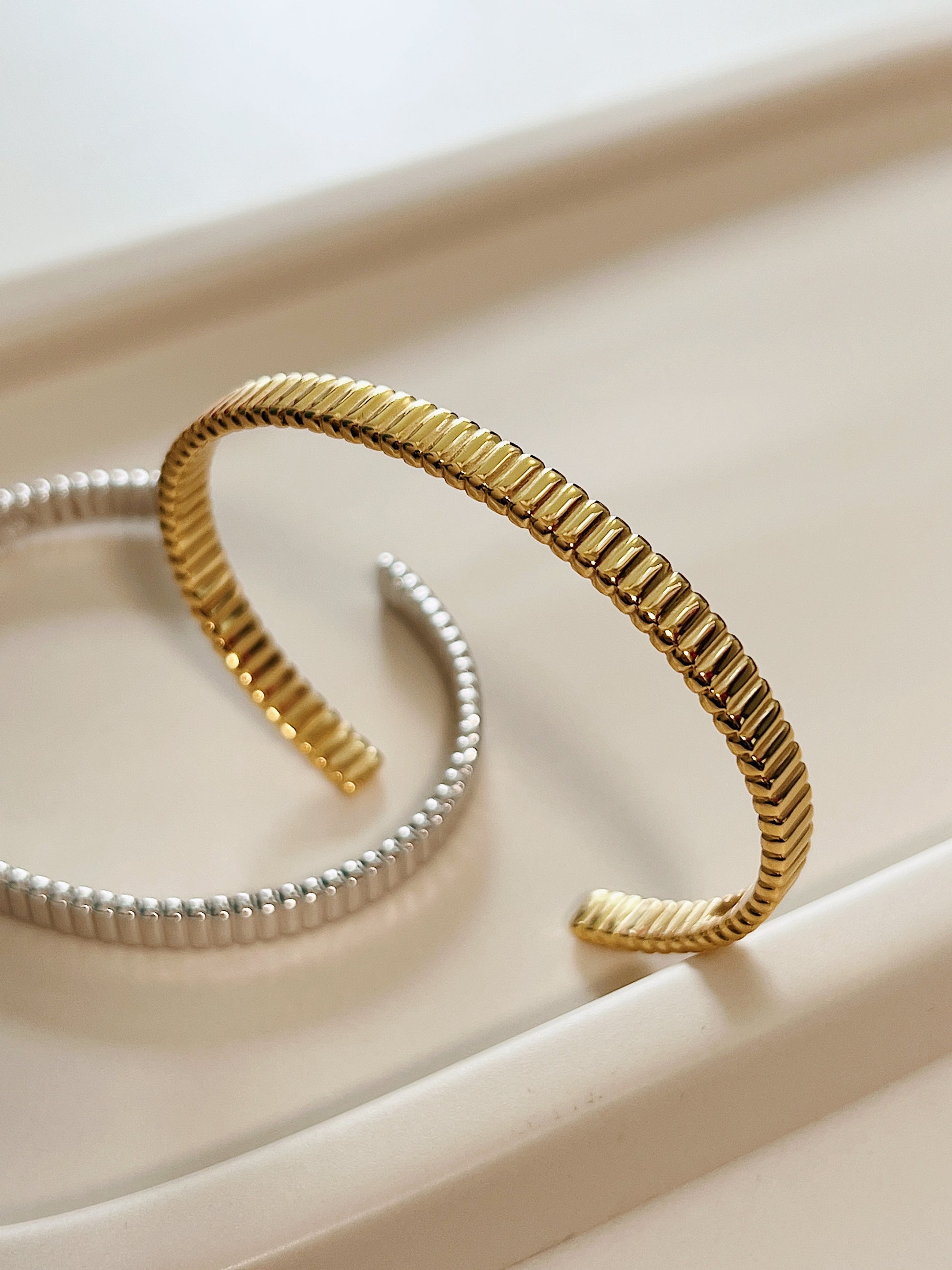 High-resolution product shot capturing the flexible opening profile of the gold vermeil flexi cuff bangle with silver at the back.