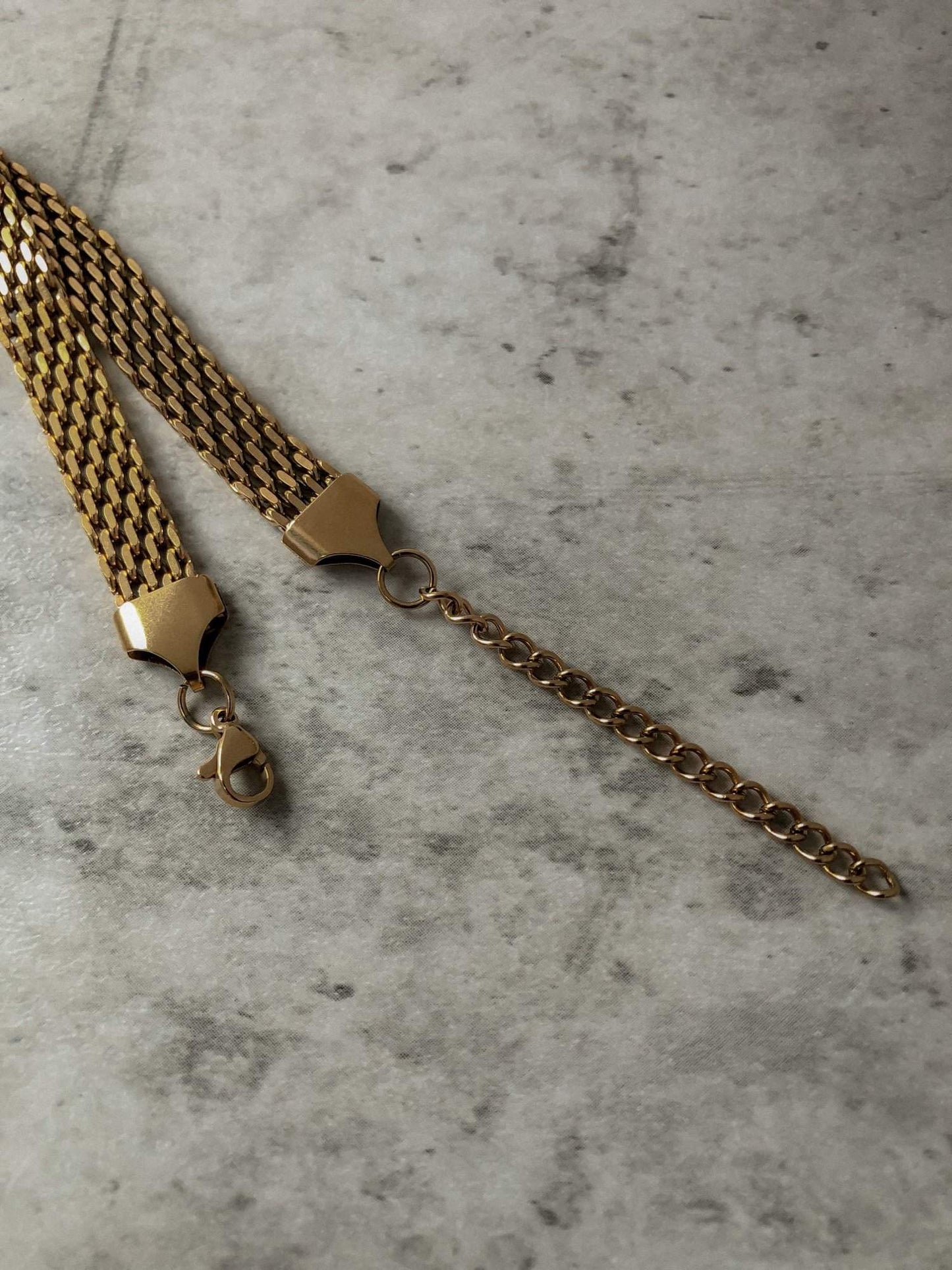 The polished anchor end caps and lobster claw closure mechanism of the Danielle gold mesh chain bracelet resting on a smooth neutral surface.