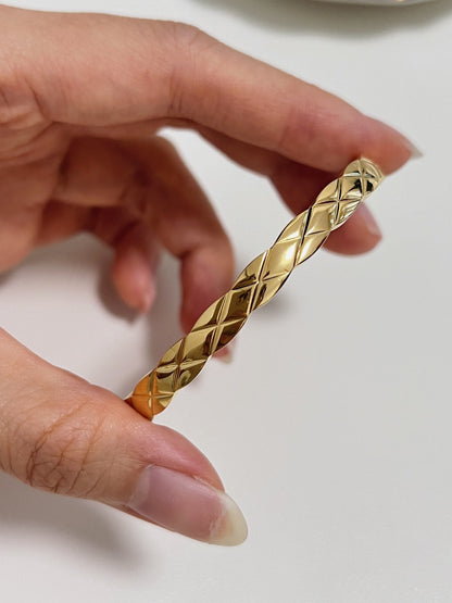 A macro close-up of a hand holding the Corin gold quilted bangle, illustrating the precise diamond-cut metal reflections and ergonomic smooth interior wall contour.