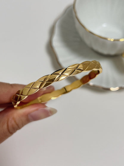 A detailed macro profile view of a hand holding the Corin gold bangle, showing the flawless light performance of its diamond-cut textured metal surface.