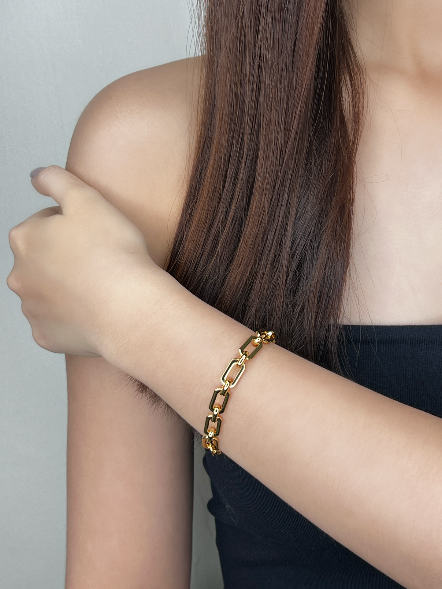 Editorial model shot showcasing the 7mm thickness of the Maia gold chain bracelet against a bare shoulder and black clothing, highlighting the premium shine.
