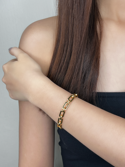 Editorial model shot showcasing the 7mm thickness of the Maia gold chain bracelet against a bare shoulder and black clothing, highlighting the premium shine.
