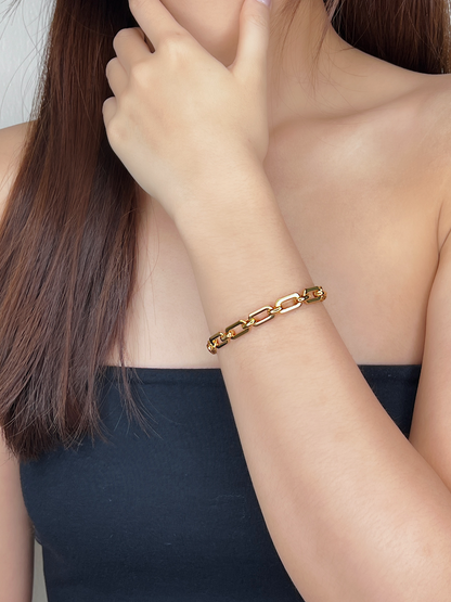 On-model view of the Maia Chunky Link Bracelet in 18K gold PVD resting flat on a wrist, styled with a minimalist strapless black top as she holds her chin.