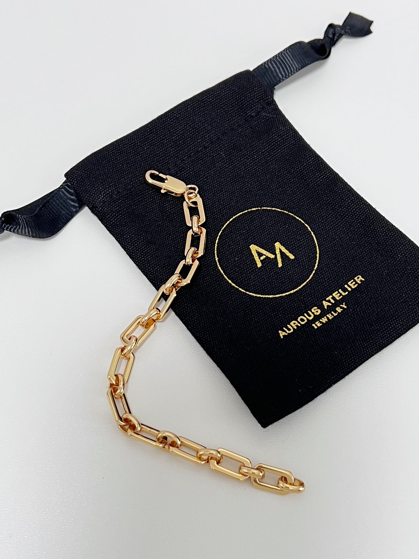 Macro product lay down of the Maia gold bracelet flat on a signature black canvas pouch, detailing the high-security custom lobster clasp and fixed 17cm loop.