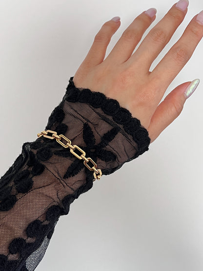 Overhead perspective of a model's open hand showcasing the continuous, uninterrupted 17cm profile of the Maia chunky gold link bracelet over sheer black lace sleeves.