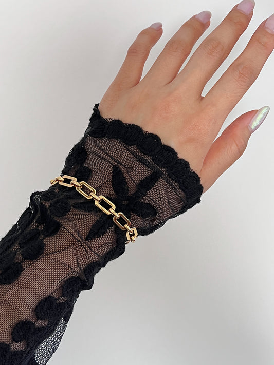 Overhead perspective of a model's open hand showcasing the continuous, uninterrupted 17cm profile of the Maia chunky gold link bracelet over sheer black lace sleeves.
