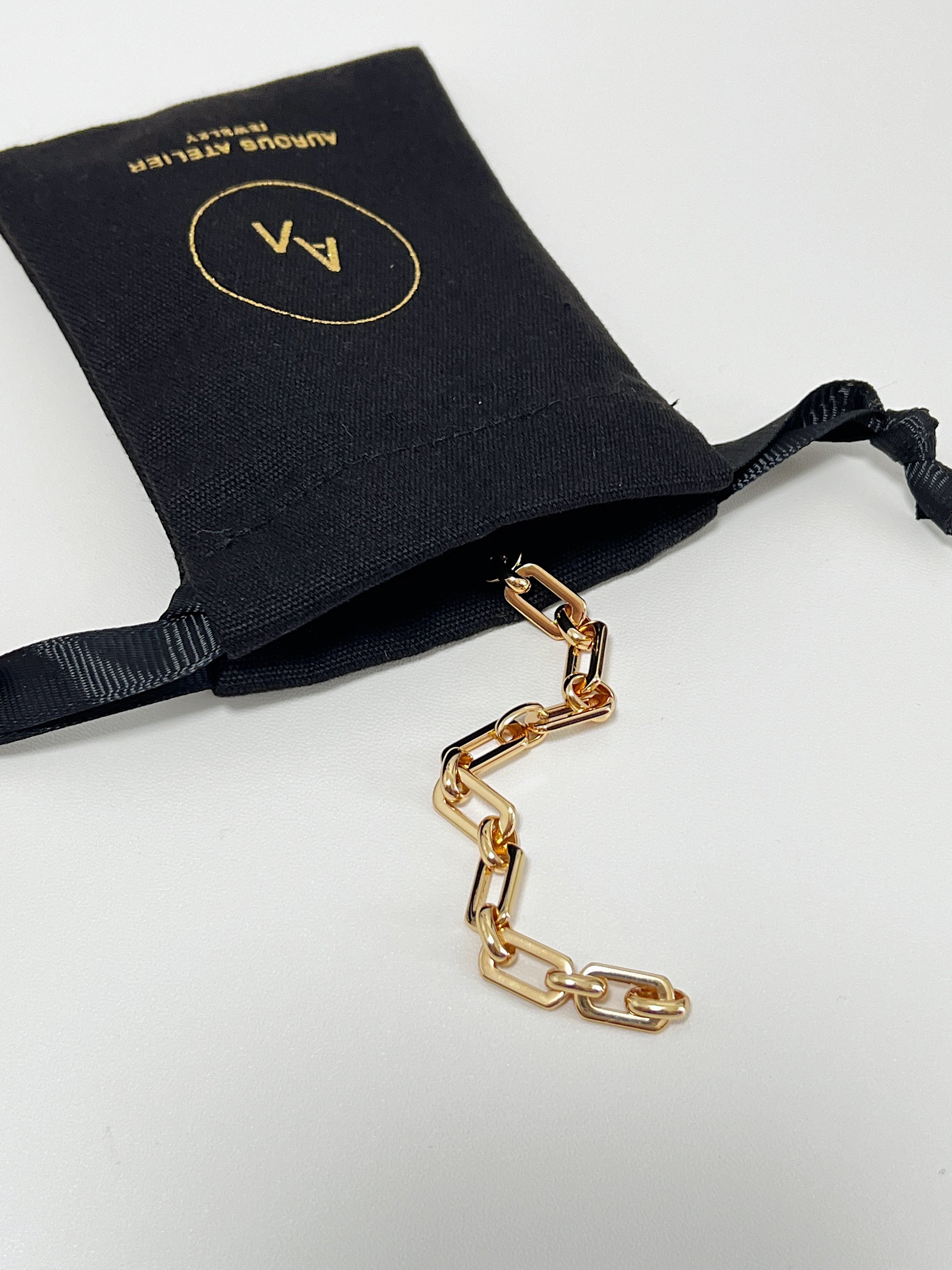 The Maia Chunky Link Bracelet coming out of a luxury black Aurous Atelier canvas drawstring jewelry pouch on a clean white surface.