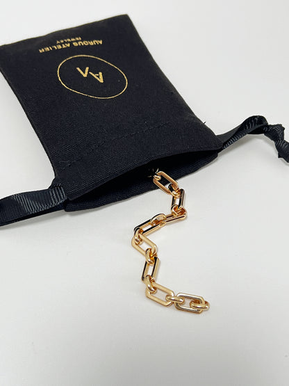 The Maia Chunky Link Bracelet coming out of a luxury black Aurous Atelier canvas drawstring jewelry pouch on a clean white surface.