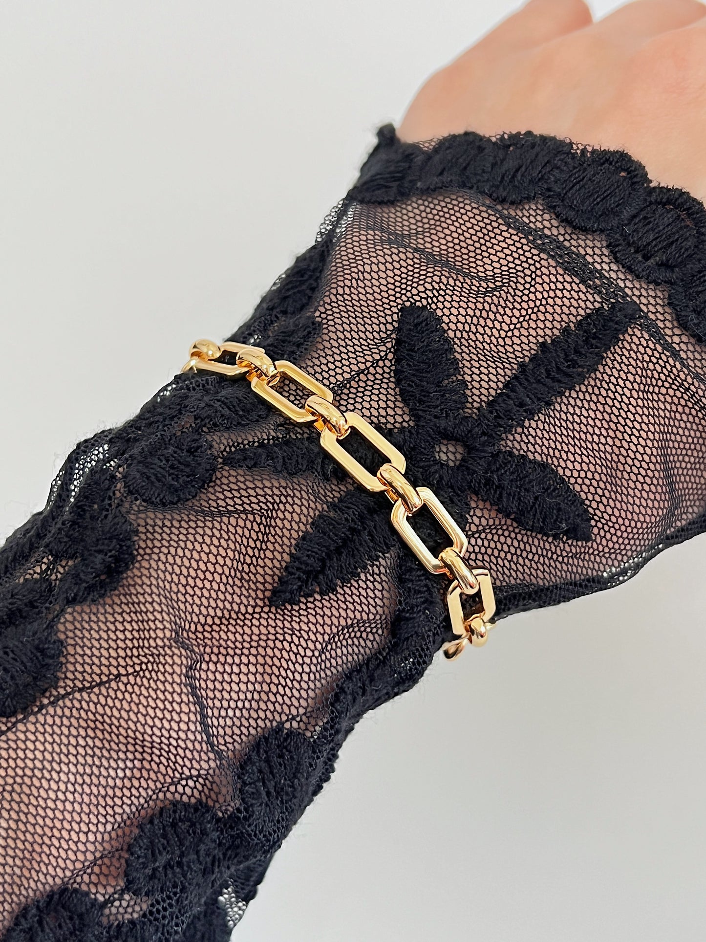 Close-up styling vignette of the Maia bold link bracelet worn over an elegant black floral lace long-sleeve bodysuit to create an avant-garde contrast.