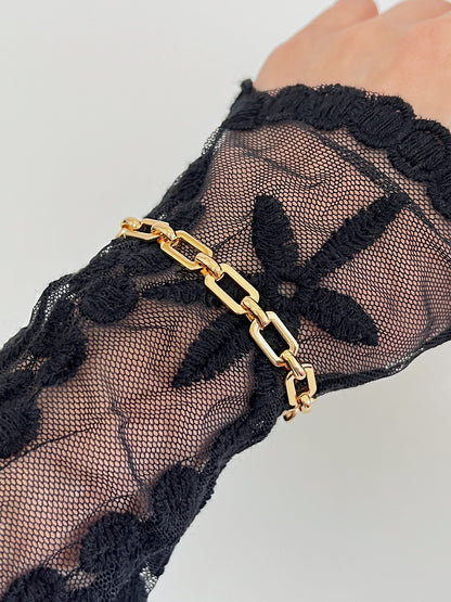 Close-up styling vignette of the Maia bold link bracelet worn over an elegant black floral lace long-sleeve bodysuit to create an avant-garde contrast.