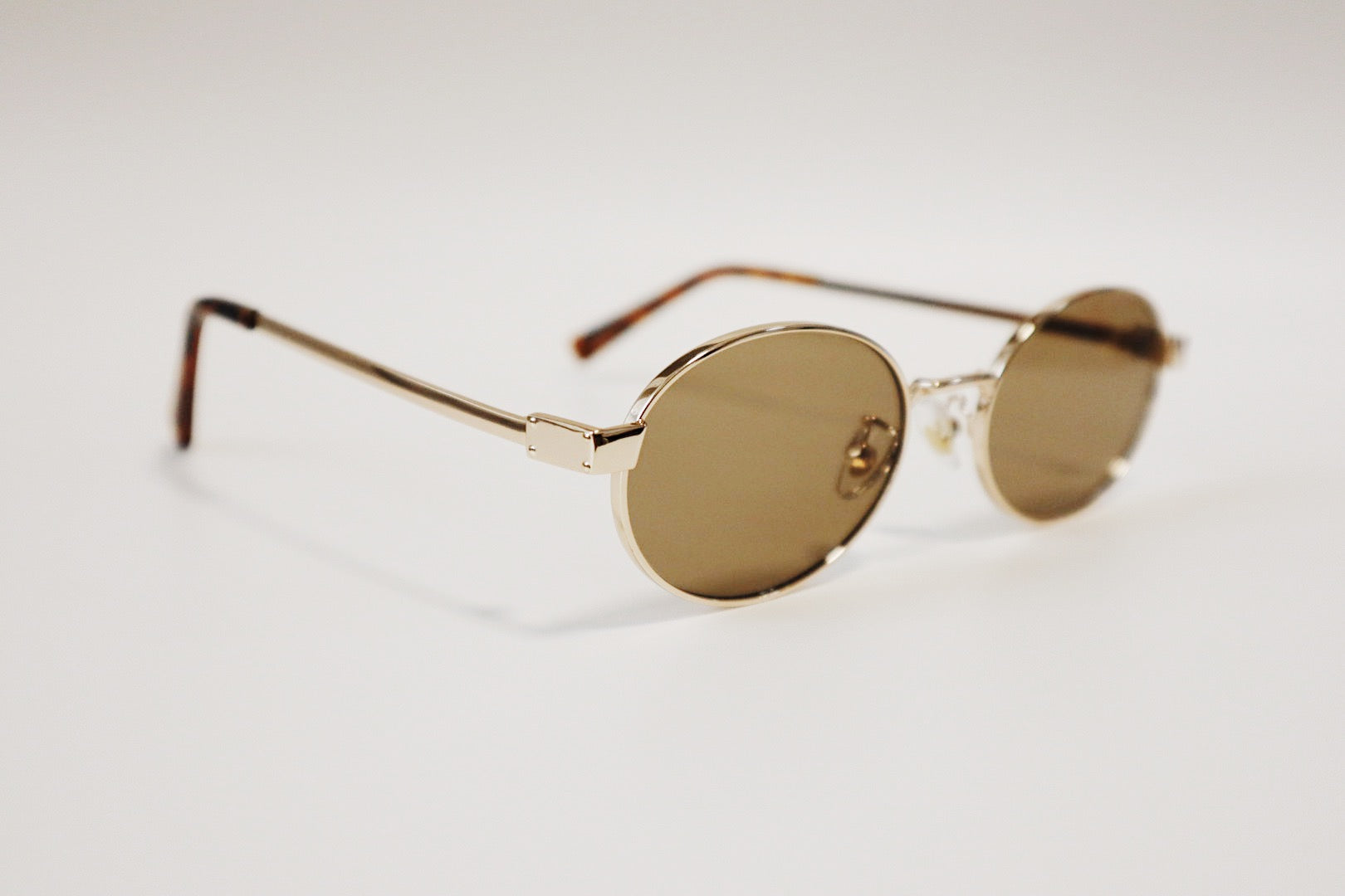 Close-up product photography of Marseille gold wire sunglasses resting at a three-quarter angle on a neutral stone surface, highlighting the smooth oval frame lines.