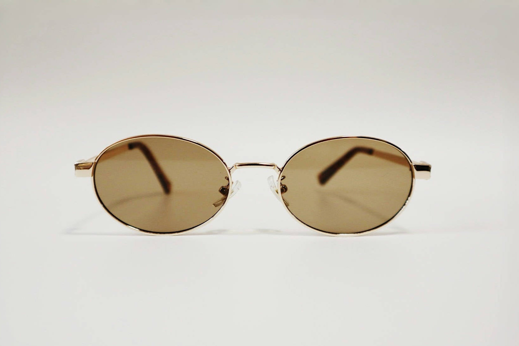 Front-facing studio product shot of Marseille refined oval sunglasses, emphasizing the balance between the gold wire frame and the warm brown tint.