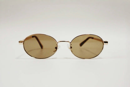 Front-facing studio product shot of Marseille refined oval sunglasses, emphasizing the balance between the gold wire frame and the warm brown tint.