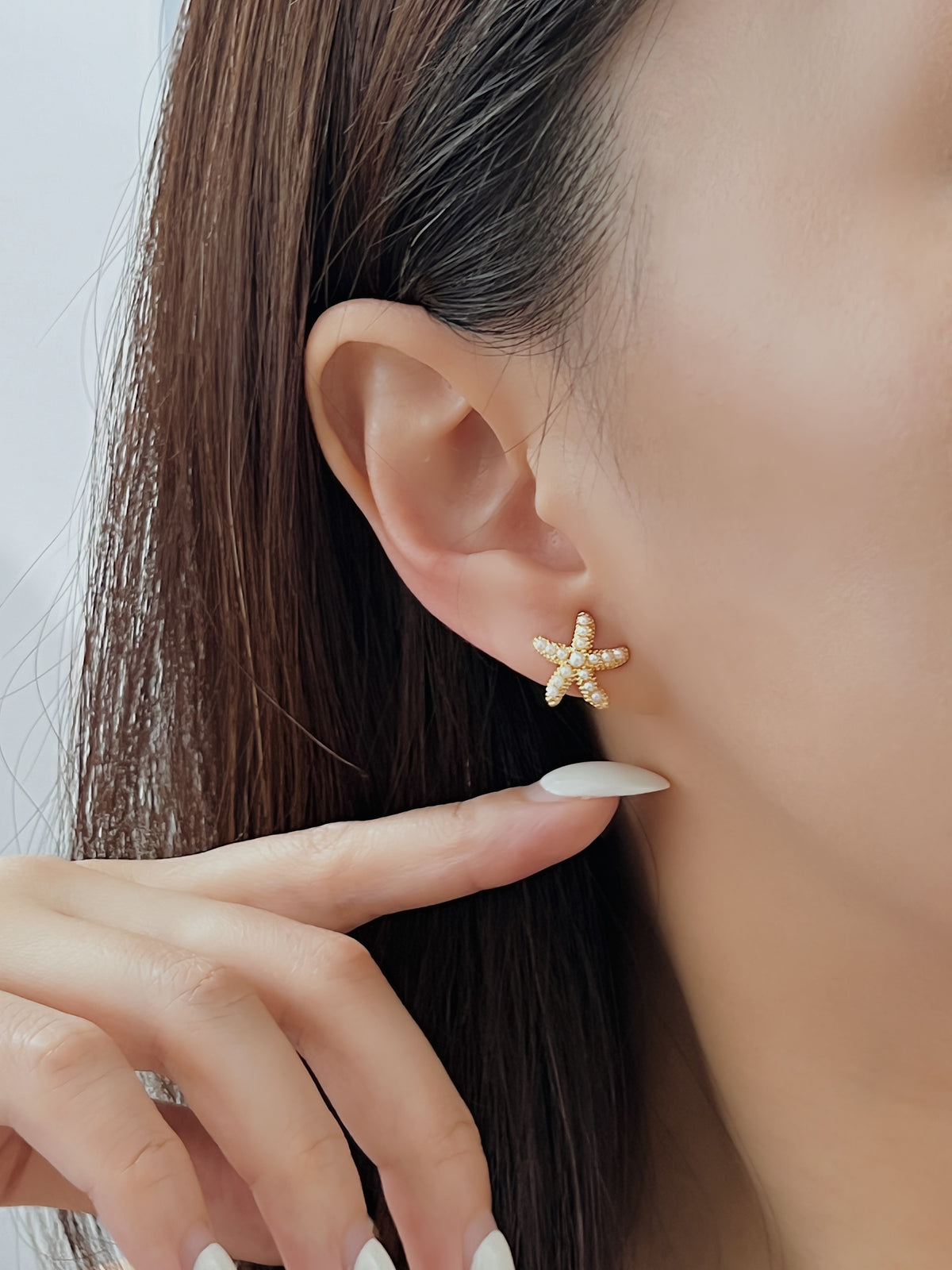 Model ear shot showing the gold pearl starfish clip-on earring resting flush against the lobe for a seamless pierced look.