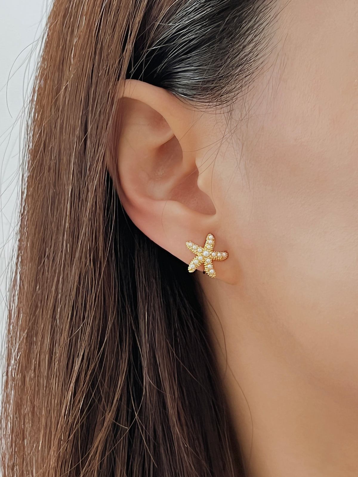 Close-up ear shot of model wearing the pearl starfish clip-on catching warm golden hour sunlight.