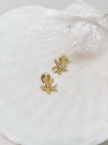 Editorial arrangement of gold starfish clip-ons resting on a textured white plaster dish for a minimalist resort look.