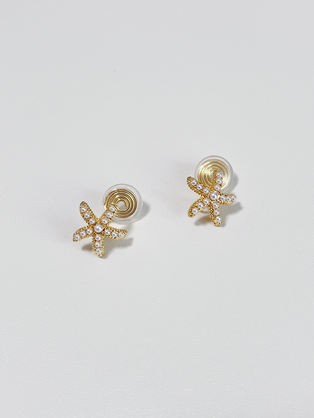 Studio flatlay display showcasing the compact 13mm starfish shape and delicate pearl detailing of the clip-on earring pair.