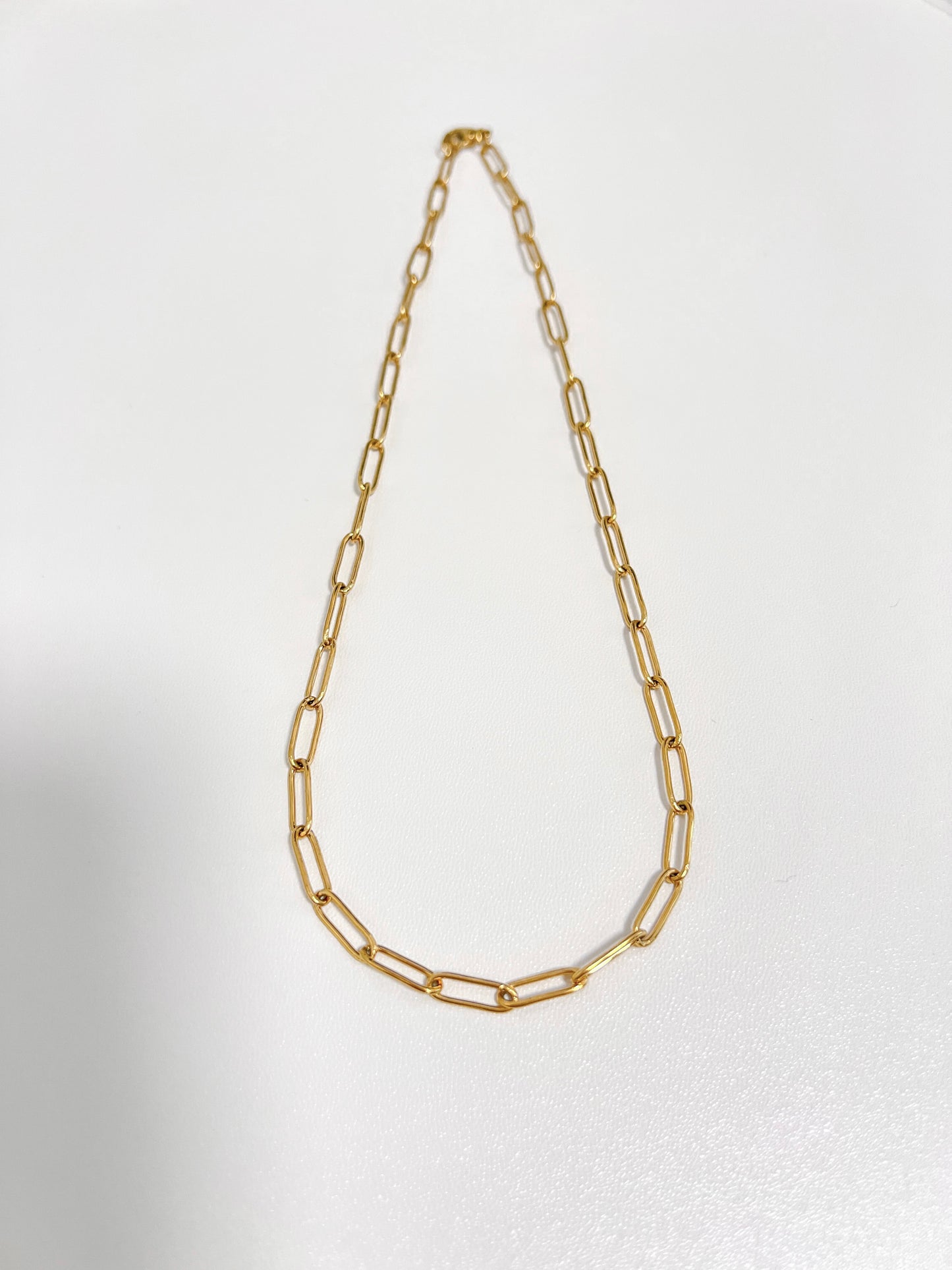Minimalist catalog layout showcasing a mid-weight golden capsule link strand resting on white surface