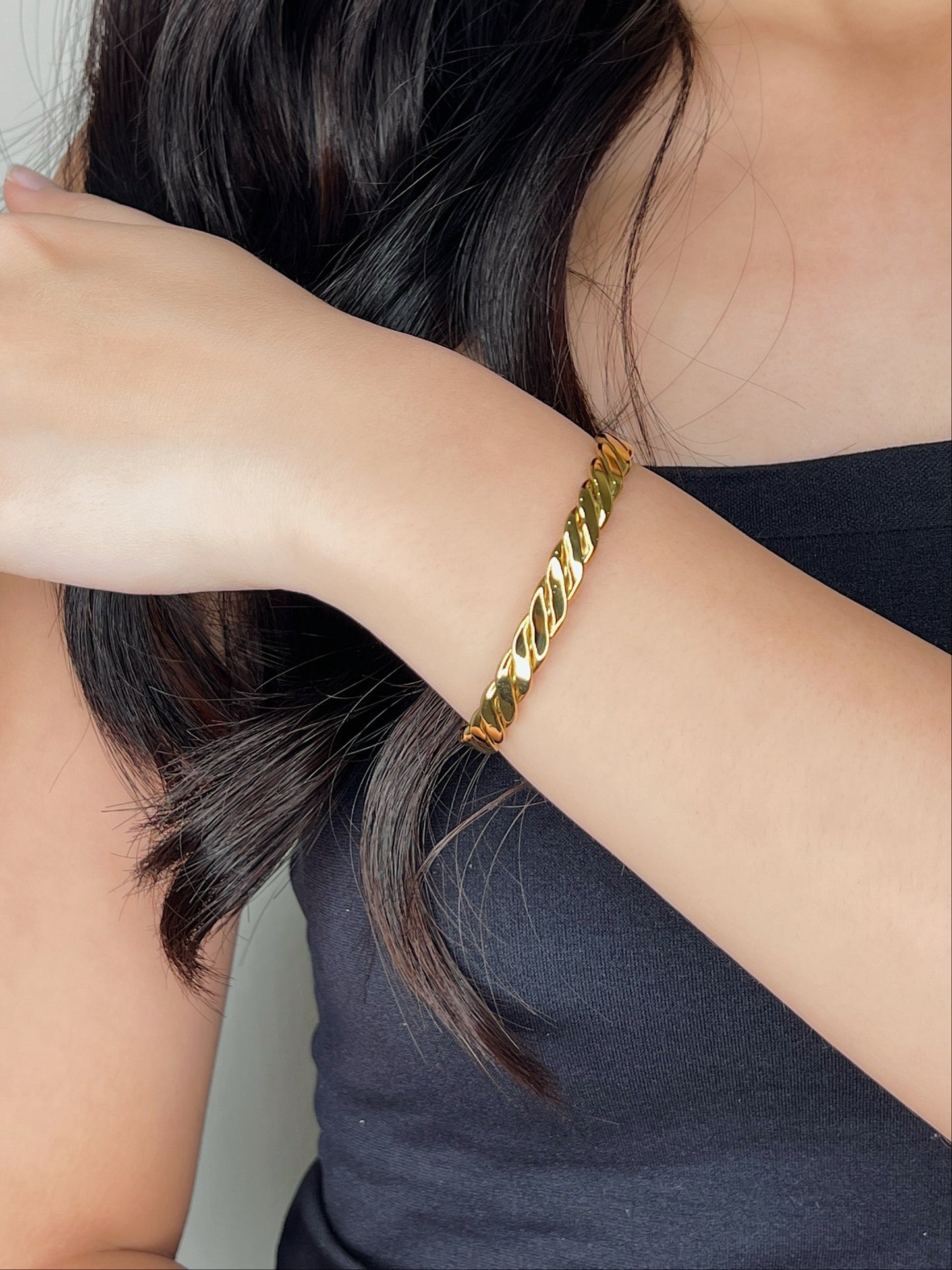 A model wearing the Mila 18k gold PVD twisted cuff bangle with her forearm resting diagonally while gently touching her dark hair